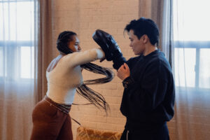 An image of a woman with long braids hitting a boxing pad with her elbow.