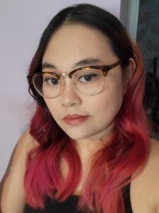 A photo of a young Asian woman with fiery pink hair and glasses.